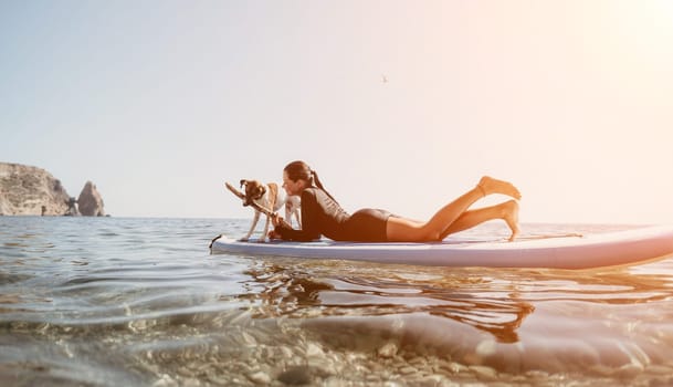 A woman lies on a paddleboard, taking a picture of a cliff in the distance. The sun shines brightly behind her.