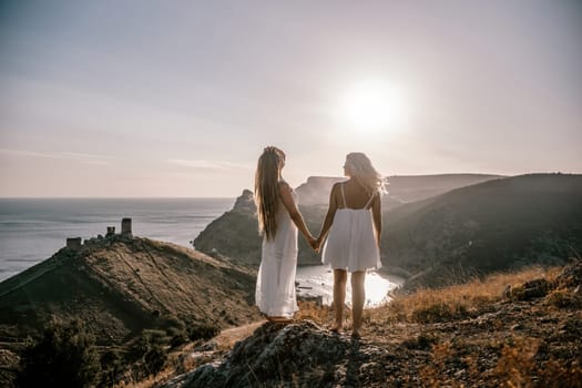 Two women are standing on a hill overlooking the ocean. They are holding hands and looking out at the water. The scene is peaceful and serene, with the sun shining brightly in the background