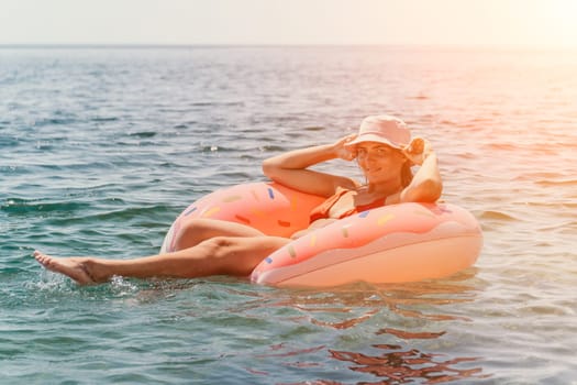 A woman relaxes on a pink flamingo float in the ocean, the sun setting behind her.