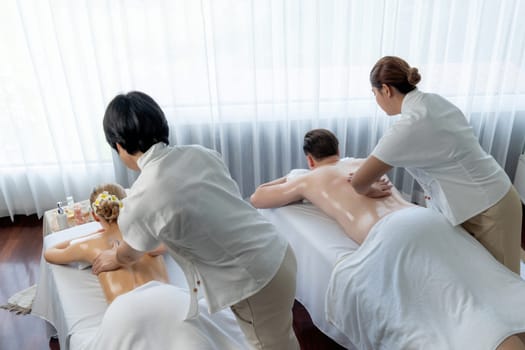 Caucasian couple customer enjoying relaxing anti-stress spa massage and pampering with beauty skin recreation leisure in day light ambient salon spa at luxury resort or hotel. Quiescent