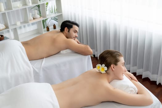 Caucasian couple customer enjoying relaxing anti-stress spa massage and pampering with beauty skin recreation leisure in day light ambient salon spa at luxury resort or hotel. Quiescent