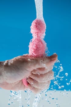 Woman holding pink anal beads under running water on blue background. Sex toy hygiene concept