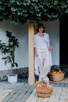 Woman dressed in casual, light-colored clothes and a wide-brimmed hat leans against a post under a leafy green canopy.