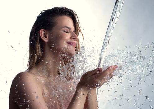 Pretty smiling girl her eyes shut enjoying water stream and splashes falling in her hands from above studio shot