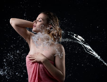 Beautiful girl her eyes shut enjoyng water stream and splashes posing against black wall
