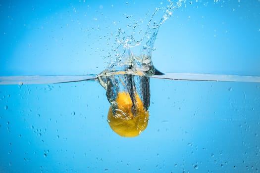 Single yellow lemon being dropped in blue water