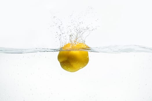 Single yellow lemon being dropped into blue water shot against white background