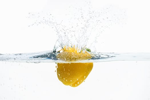 Sweet yelllow pepper thrown in water from top with splashes above it