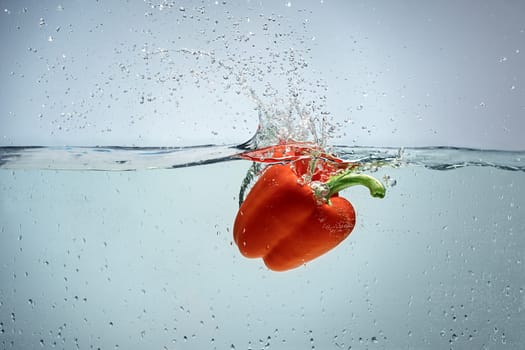 Single red pepper being dropped in blue water