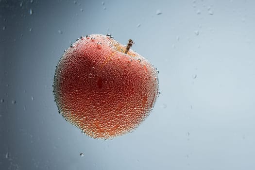 Single red apple covered with air bubbles floating in blue water