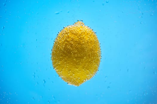 Yellow lemon floating in blue water and covered by air bubbles