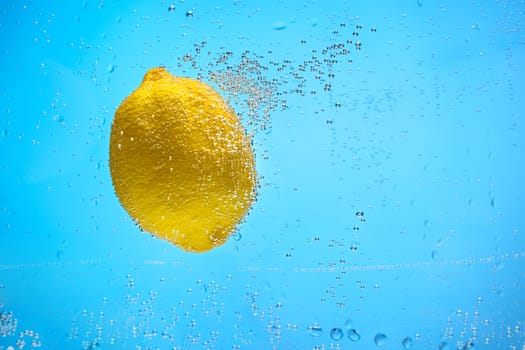 Single yellow lemon covered with air bubbles floating in blue water