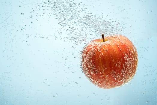 Sweet red apple floating in water and covered by air bubbles
