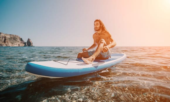 A man paddles a stand up paddle board in the ocean. The sun is setting and the water is calm.