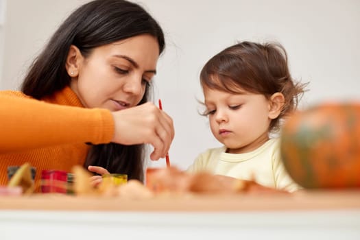 happy little child girl and her mother drawing for the autumn holiday. Happy family making autumn decorations together