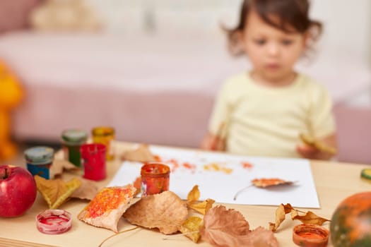 happy little child girl painting autumn leaves. baby girl drawing leaves in yellow and orange paint