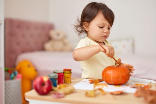 happy little child girl painting Halloween pumpkin. smiling baby girl drawing autumn pumpkin in yellow paint
