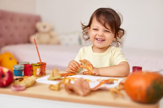 happy little child girl painting autumn leaves. baby girl drawing leaves in yellow and orange paint