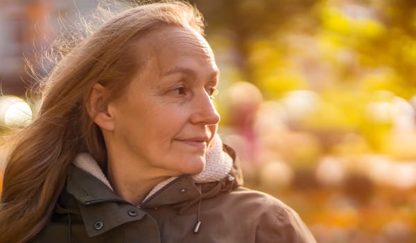 An elderly 60 beautiful woman with a kind smile is walking outdoors on a sunny autumn day, a happy old lady, a grandmother takes care of her appearance, natural beauty with wrinkles portrait closeup.