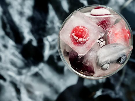 Glass with ice cubes with frozen berries and fruits close-up for a refreshing drink and preservation of seasonal vitamins raspberries, strawberries, cherries, blueberries, mulberries, blackberries