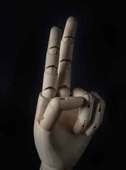 Wooden hand of mannequin with raises two fingers on dark background. Positive concept, Wooden hand puppet, Showing, Symbol, Banner design, Gesture and sign, Space for text, Selective focus.