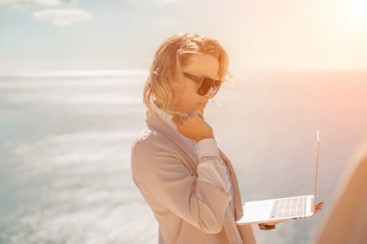 Freelance women sea working on the computer. Good looking middle aged woman typing on a laptop keyboard outdoors with a beautiful sea view. The concept of remote work