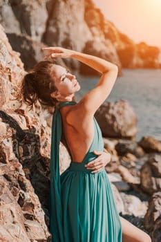 Woman green dress sea. Woman in a long mint dress posing on a beach with rocks on sunny day. Girl on the nature on blue sky background