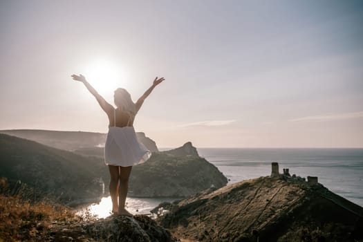 A woman is standing on a hill overlooking a body of water. She is wearing a white dress and she is happy