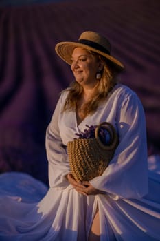 Woman poses in lavender field at sunset. Happy woman in white dress holds lavender bouquet. Aromatherapy concept, lavender oil, photo session in lavender.