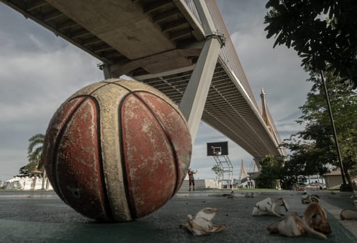 Basketball ball on the Old cement court floor at Outdoor park with Suspension bridge and Sky in the background. Copy space, Selective focus.