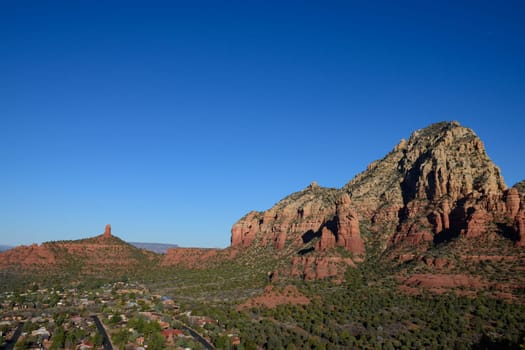 A breathtaking view of Sedona, Arizona, showcasing its iconic red rock formations set against a clear blue sky. The image captures a quiet residential area nestled among the dramatic desert landscape.