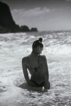 A woman in a stylish bikini enjoys ocean waves, captured in classic black and white, evoking elegance and tranquility