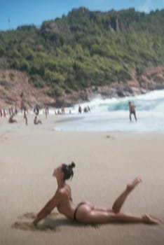 A tranquil beach setting shows a person peacefully practicing yoga beside the soothing waves while wearing a bikini