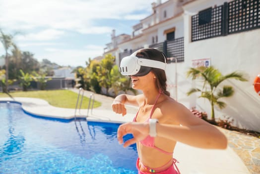 A young woman wearing VR goggles joyfully plays and interacts by the sunny poolside, merging technology with leisure