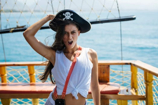 A spirited young woman dressed as a pirate poses playfully aboard a ship with open waters behind her.