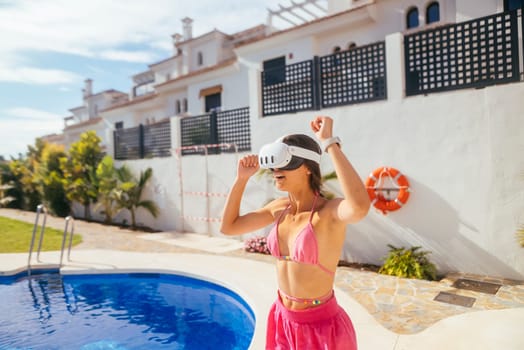 A joyful woman in a bright pink outfit enjoys VR fun by a sunny pool, merging summer vibes with exciting tech