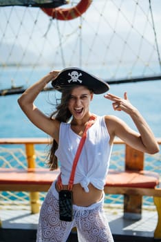 A young woman playfully wears a pirate hat, enjoying her vibrant life aboard a ship with a beautiful ocean view