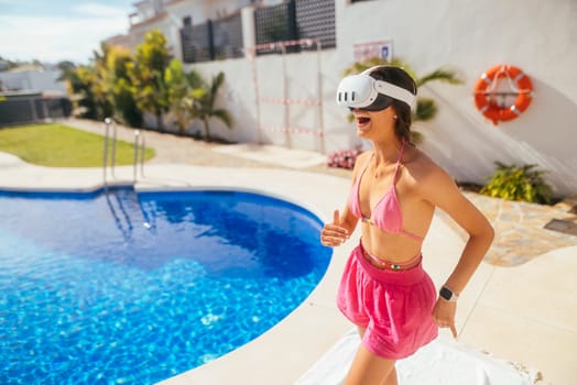 A girl in a colorful bikini is enjoying a fun virtual reality experience by the pool on a sunny day