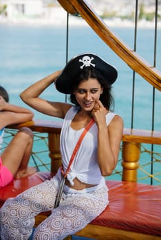 A joyful woman in a stylish pirate hat enjoys the deck of a ship, surrounded by stunning ocean views