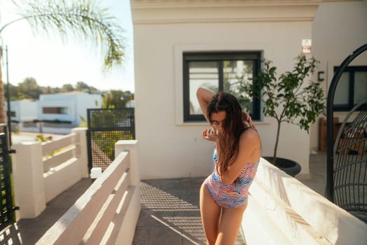 A cheerful woman in a vibrant and colorful swimsuit is relaxing by a stylish and inviting poolside under the warm sun