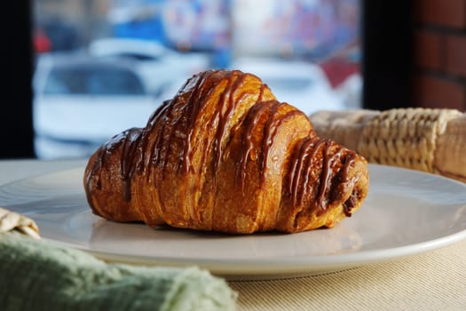 Golden brown croissant sits invitingly on a plate beside a textured linen napkin in a cozy setting