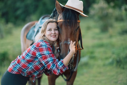 Happy blonde with horse in forest. Woman and a horse walking through the field during the day. Dressed in a plaid shirt and black leggings