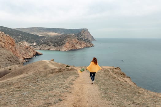A woman is walking on a path near the ocean. She is carrying a bouquet of flowers