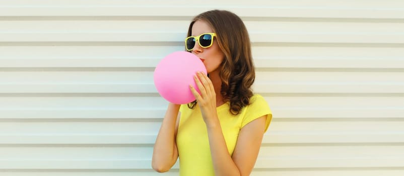 Fashion colorful portrait of stylish cool young woman inflating pink chewing gum or balloon, teenage girl in yellow glasses on white background
