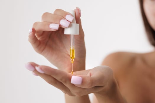 Close up of woman applying organic face and body oil with pipette, dripping a drop of oil onto her palm,