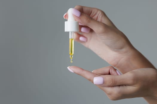 Close up of woman applying organic face and body oil with pipette, dripping a drop of oil onto her palm,