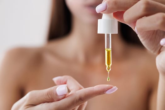 Beautiful girl dripping skin care product on her finger with a pipette, close-up, vitamins or natural oils on a white isolated background