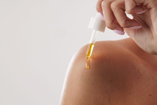 woman applying oil and serum on body with pipette close-up, on white background, concept of body and skin care