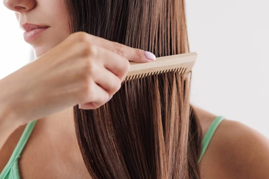 Close up of woman combing her long straight brown hair with wooden comb. hair care, hair problem