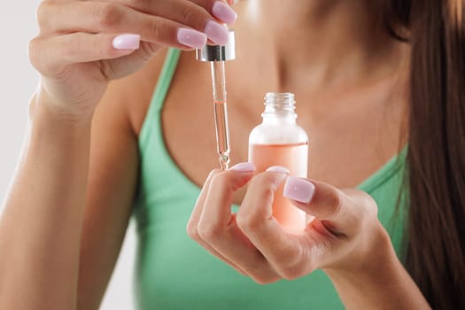 woman applying organic oil on cuticles with pipette close-up, hand care concept, healthy nails and skin